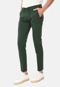 Chino in cotone verde con gambe affusolate, tasche frontali e chiusura con bottone. Abbinati a sneaker bianche con suola in cuoio.