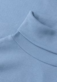 Jasnoniebieski, prążkowany golf o gładkiej fakturze, dopasowanym kroju i złożonym kołnierzem. Faktura podkreśla głębię wizualną.