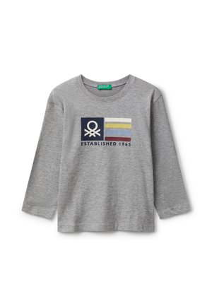 Camicia grigia a maniche lunghe con un logo che presenta un simbolo bianco su un quadrato blu navy accanto a quattro strisce orizzontali colorate e il testo "Fondato nel 1965".