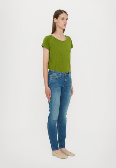 Grønn kortermet skjorte kombinert med lyseblå skinny jeans og beige leppestift, med enkel design og klassisk denimtekstur.