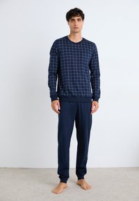 Ensemble de pyjama bleu marine avec motif à carreaux. Haut à manches longues avec col rond et poignets côtelés, associé à un pantalon ample assorti. Texture de tissu douce.