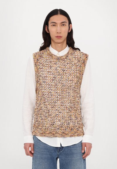 Pull sans manches en laine multicolore avec un motif texturé. Porté par-dessus une chemise blanche à col, avec un décolleté arrondi.