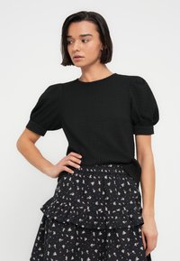 Μαύρο τοπ με υφή και φουσκωτά μανίκια, συνδυασμένο με μαύρη φούστα με λουλουδένιο σχέδιο, βολάν και ελαστική μέση.