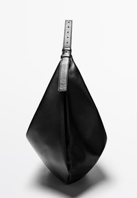 Sac souple en cuir noir avec une seule bandoulière réglable suspendu sur fond blanc.