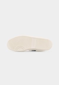 Zool van een witte schoen met een gestructureerd patroon bestaande uit horizontale groeven en kleine verhoogde rechthoeken voor grip.