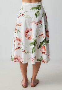 Blumiger Midirock aus weißem Stoff, mit pinken und grünen Blumenmustern, ausgestelltem Design und glatter Oberfläche. Endet unterhalb des Knies.