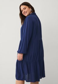 Vestido midi azul marino hecho de una tela ligera, con mangas largas, un cuerpo plisado y un diseño de falda en capas.