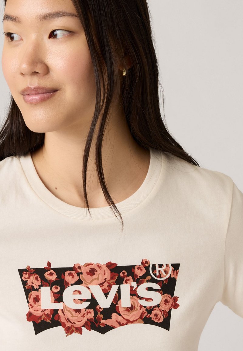 Cremfarbener T-Shirt mit floralem Grafikdesign in Rosa- und Rottönen, auf schwarzem Hintergrund mit weißem "Levi's" Textlogo.