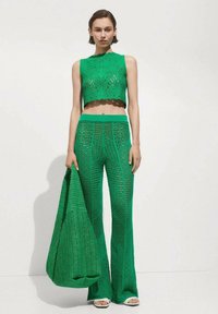 Grüner gestrickter Cropped-Top und weit geschnittene Hose im Set mit gewellten Kanten und durchbrochenen Mustern, kombiniert mit einer passenden grünen Tasche.