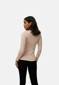 Top de manga larga rosa claro con cuello redondo y diseño ajustado. Textura suave, combinado con pantalones ajustados negros.