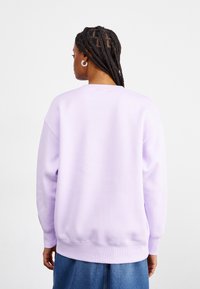 Sweatshirt lilás com um corte relaxado, punhos e bainha canelados. Textura suave, estilo pullover e design minimalista.