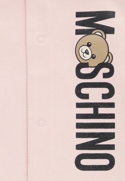 Tessuto rosa con il testo nero "MOSCHINO" e un volto di orsacchiotto cartoon integrato nel design, con bottoni a pressione visibili.