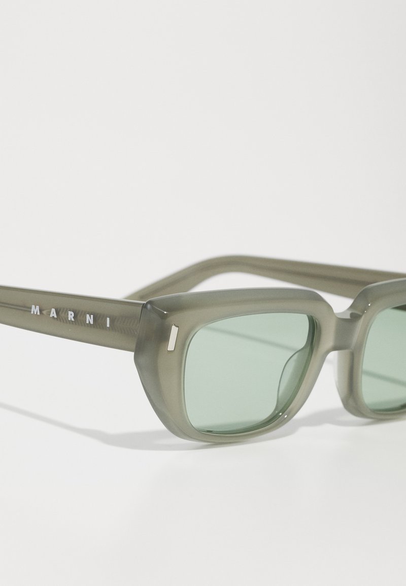 Graugrüne Sonnenbrille mit einem massiven, quadratischen Rahmen, der aus transparentem Acetatmaterial besteht und dezente Logodetails an den Bügeln aufweist.