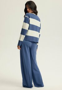 Niebiesko-biały pasiasty longsleeve z luźnym krojem, zestawiony z luźnymi niebieskimi spodniami, obydwa wykonane z miękkiego, gładkiego materiału.