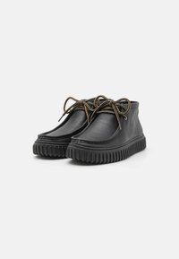 Chaussures en cuir noir avec une tête arrondie, lacets bruns et une semelle épaisse en caoutchouc striée. Présente des coutures simples le long des bords.