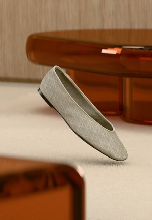 Μπεζ μπαλαρίνα με γεωμετρικό μοτίβο αιωρείται πάνω από ένα ανοιχτό χαλί σε ένα σύγχρονο δωμάτιο με έπιπλα σε κεχριμπαρένιους τόνους.