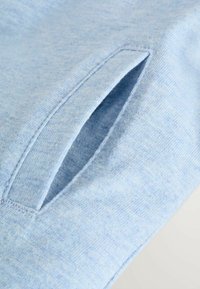 Felpa azzurra con una texture morbida e un'apertura per tasca laterale, rifinita con cuciture ordinate. Il tessuto presenta un delicato motivo melangiato.