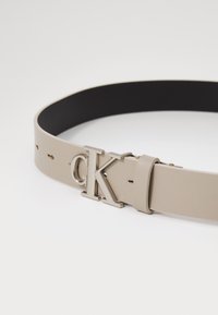 Beige műbőr öv matt felülettel, ezüst CK logós csattal és fekete belső résszel, letisztult, minimalista kinézetre tervezve.
