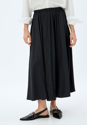 Rok hitam sepanjang pergelangan kaki dengan pinggang elastis, memiliki tekstur halus dan desain yang mengalir. Dipadukan dengan sepatu hitam berhak datar.