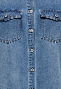 Light blue denim shirt featuring a button front, two chest pockets with flaps, and silver-tone snap buttons. Smooth texture with subtle stitching.