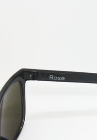 Mustat aurinkolasit tummilla linsseillä, joissa on sileä pinta ja näkyvä brändimerkintä "Rose" kehystyypin sivussa.