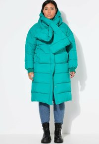 Teal pufferjakke med et stort tørklæde, med lynlås fortil og to sidelommer. Materialet er quiltet, med ribbede manchetter og en afslappet pasform.