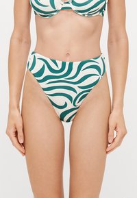 Visoke bikinice s zelenim valovitim vzorcem na krem ozadju, gladek material in čist dizajn, z nastavljivimi naramnicami in izrezanimi stranmi.