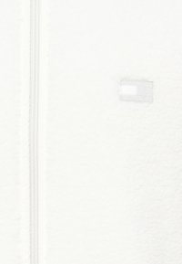 White fleece jacket featuring a textured surface, a front zipper, and a small label on the right side with a rectangular pattern.
