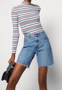 Haut à manches longues à rayures de couleurs pastel avec une texture côtelée, associé à un short en denim bleu clair avec des bords effilochés et cinq poches.