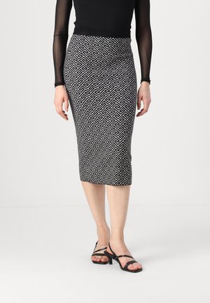 Kvinde iført en sort og hvid knælængde pencilskørt med geometrisk mønster, gennemsigtig sort bluse med lange ærmer og sorte sandaler med stropper.
