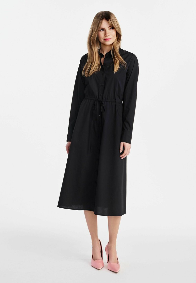 Czarna sukienka z długim rękawem, zapinana na guziki, z regulowanym paskiem w talii i spódnicą o długości midi. Stylizowana z różowymi szpilkami. Gładka faktura.