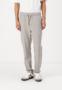 Helle graue Jogginghosen aus einem strukturierten Material, mit einem elastischen Bund und Kordelzug sowie seitlichen Taschen. Kombiniert mit weißen Sneakern.