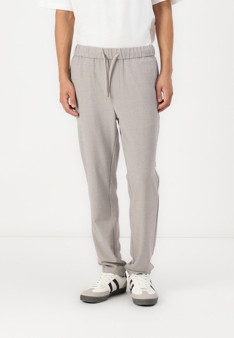 Helle graue Jogginghosen aus einem strukturierten Material, mit einem elastischen Bund und Kordelzug sowie seitlichen Taschen. Kombiniert mit weißen Sneakern.