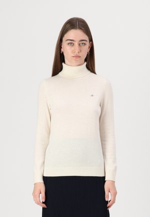 Pull col roulé crème avec manches longues, texture douce et motif dégradé subtil vers le bas. Petit logo sur la poitrine.
