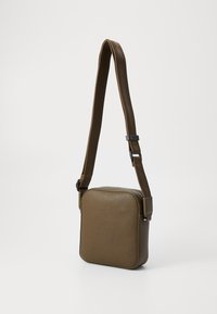Brun struktureret læder crossbody taske med kvadratisk form, justerbar stofrem og metal lynlås. Minimalistisk design med diskrete detaljer.
