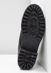 Semelle de botte noire avec une semelle profonde, présentant des motifs d'étoile et de chevrons, taille 37, sur fond blanc avec coins.