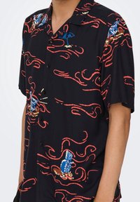 Korte mouwen zwarte shirt met rode en blauwe golfpatronen, met geborduurde paraplu's en ananassen. Met knoopsluiting aan de voorkant en een casual kraag.