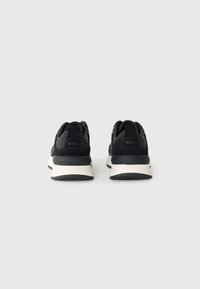 Sorte sneakers med en blanding av materialer, inkludert skinn og tekstil, med en kremfarget mellomsåle og svart yttersåle. Logo på hælen.