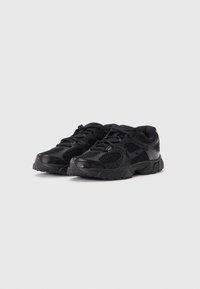 Baskets de sport noires avec un dessus en mesh, fermeture à lacets, col rembourré et semelle en caoutchouc texturé avec un motif de dentelle visible.