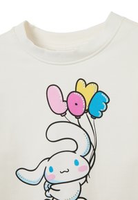 Camiseta blanca de algodón con un dibujo de un conejo de dibujos animados sosteniendo tres globos coloridos en rosa, amarillo y azul, con un contorno y acentos en negro.