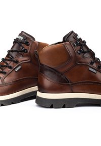 Botas de senderismo de cuero marrón con un collar alto, cordones negros, suela de goma y detalles en contraste para mayor durabilidad y soporte.