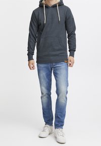 Haut à capuche gris foncé avec une doublure gris clair, cordons ajustables et poche avant. Assorti avec un jean bleu clair et des baskets blanches.