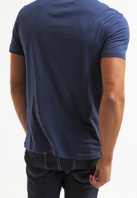 Mörkblå bomullströja med korta ärmar och rundad halsringning, figursydd design, slät yta, bärs med mörka jeans.