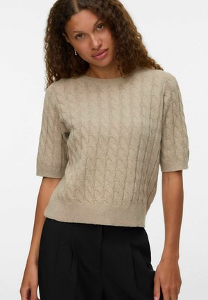 Beige kortärmad tröja med ett flätat mönster, ribbad halsringning och nederkant, tillverkad av mjukt material, kombinerad med svarta byxor.