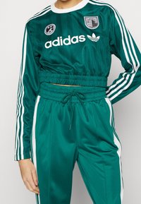 Grön satin Adidas träningsoverall med vita ränder, kort topp med elastisk midja, matchande byxor och broderade logotyper.