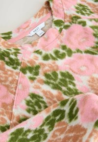 Weicher Stoff mit flauschiger Textur, der ein florales Muster in Rosa-, Grün- und Beigetönen zeigt, sowie einem runden Ausschnitt mit einer genähten Nahtdetail.
