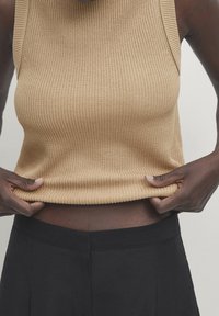 Beige ribberknit sleeveless top med en tætsiddende design, der fremhæver teksturen. Toppen bæres over højtråddede sorte bukser.
