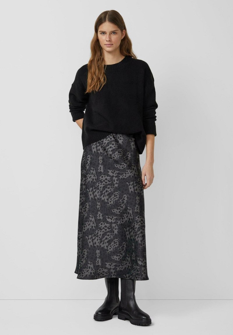 Zwarte oversized trui gecombineerd met een lange, donker gemusterde rok met een bladerenontwerp. Zwarte kniehoge laarzen maken de look compleet.