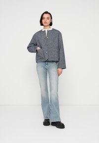 Μπλε σακάκι από τουίντ με στρογγυλή γιακά, κουμπιά μπροστά και δύο τσέπες, συνδυασμένο με ανοιχτόχρωμο τζιν καμπάνα και μαύρα μποτάκια με πλατφόρμα.