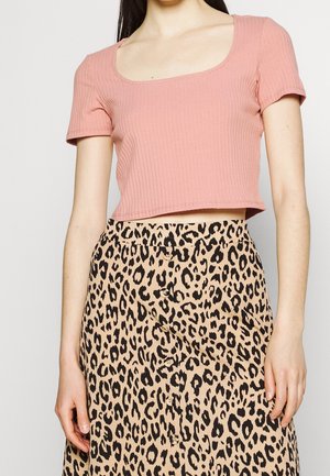 Femme portant un haut court côtelé rose à manches courtes associé à une jupe taille haute beige à imprimé léopard avec des boutons sur le devant.